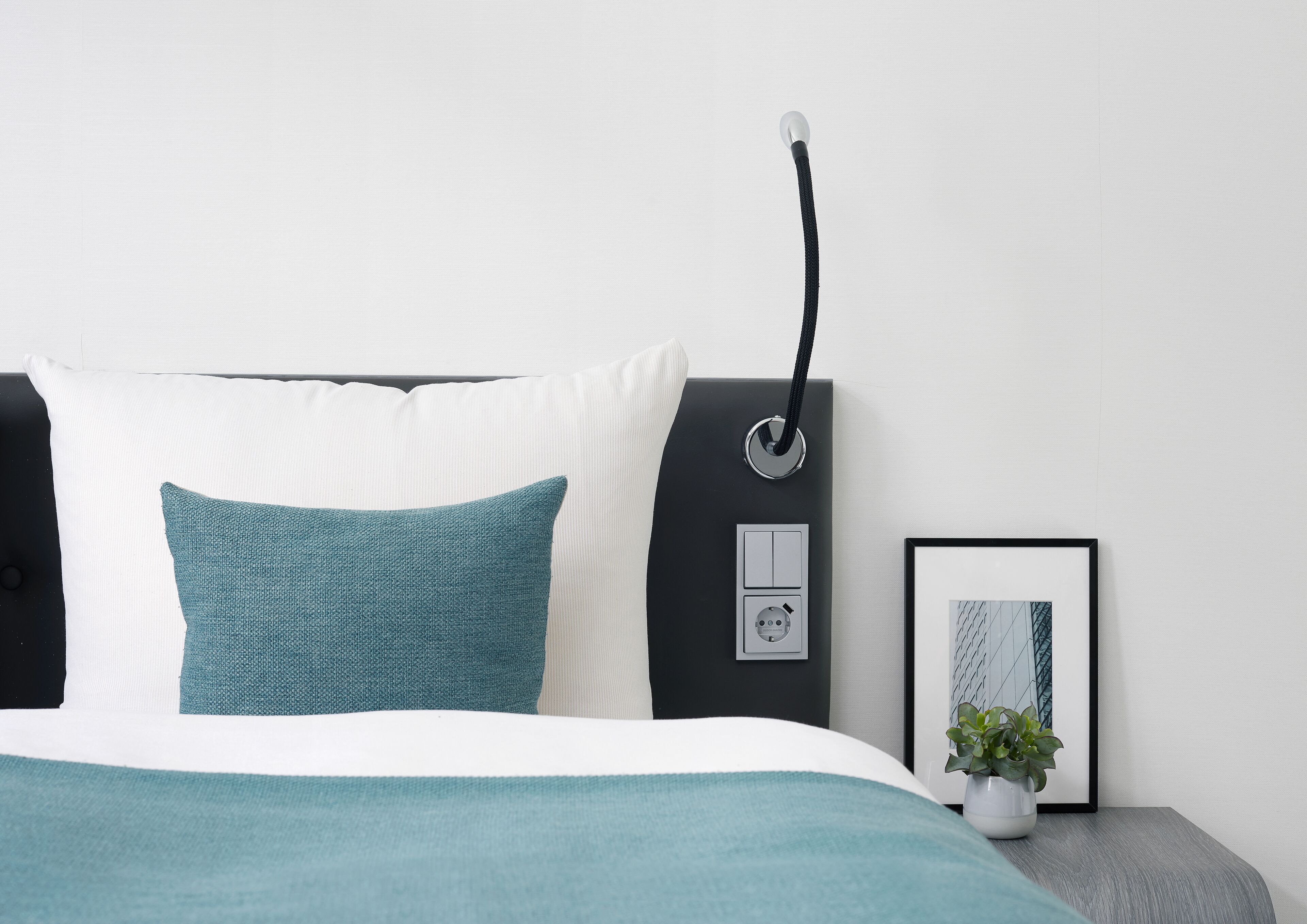 A modern bedroom with a bed, a bedside table with a lamp, and a framed picture.