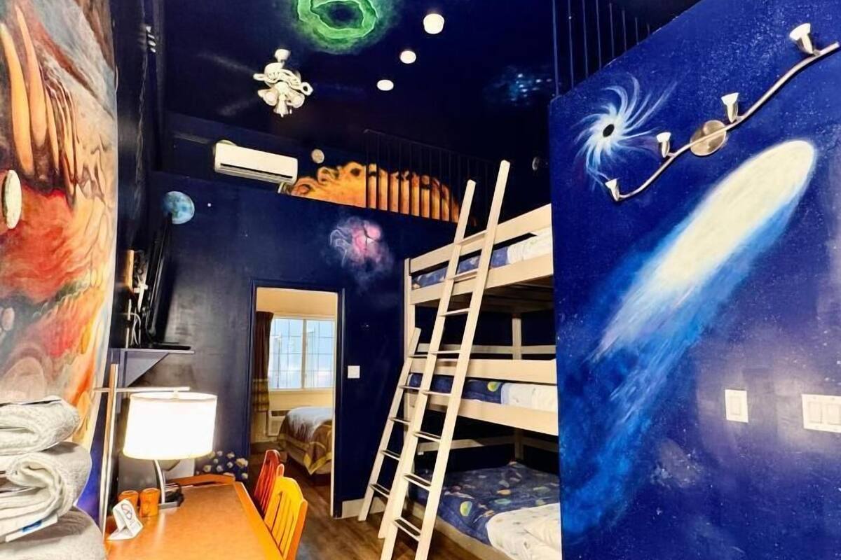 A room with bunk beds, a desk with a lamp, and a mural of space.