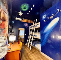 Una habitación con literas, un escritorio con lámpara y un mural del espacio.