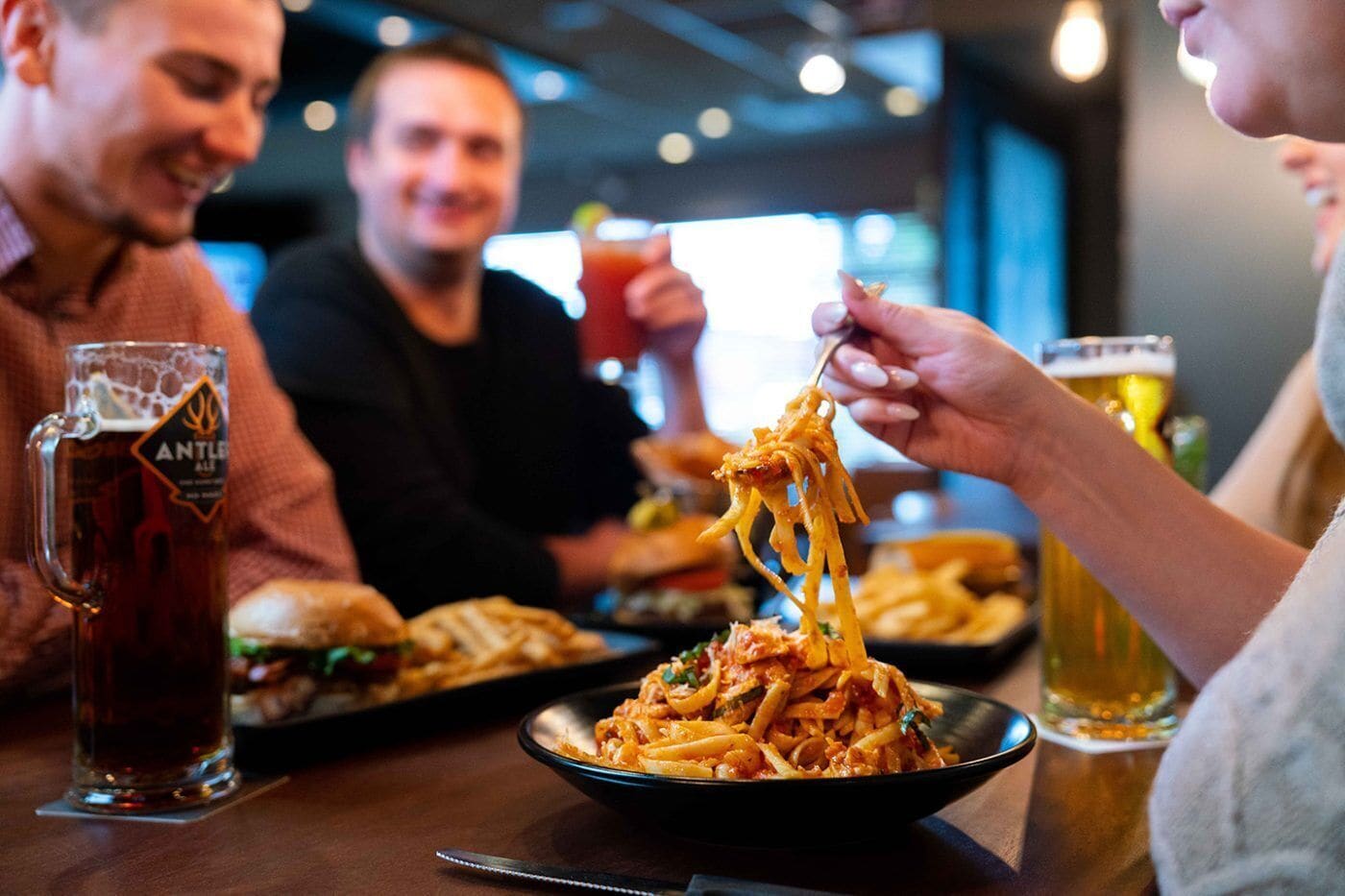 Une table à manger avec une assiette de spaghettis, un pichet à bière et un verre de bière.