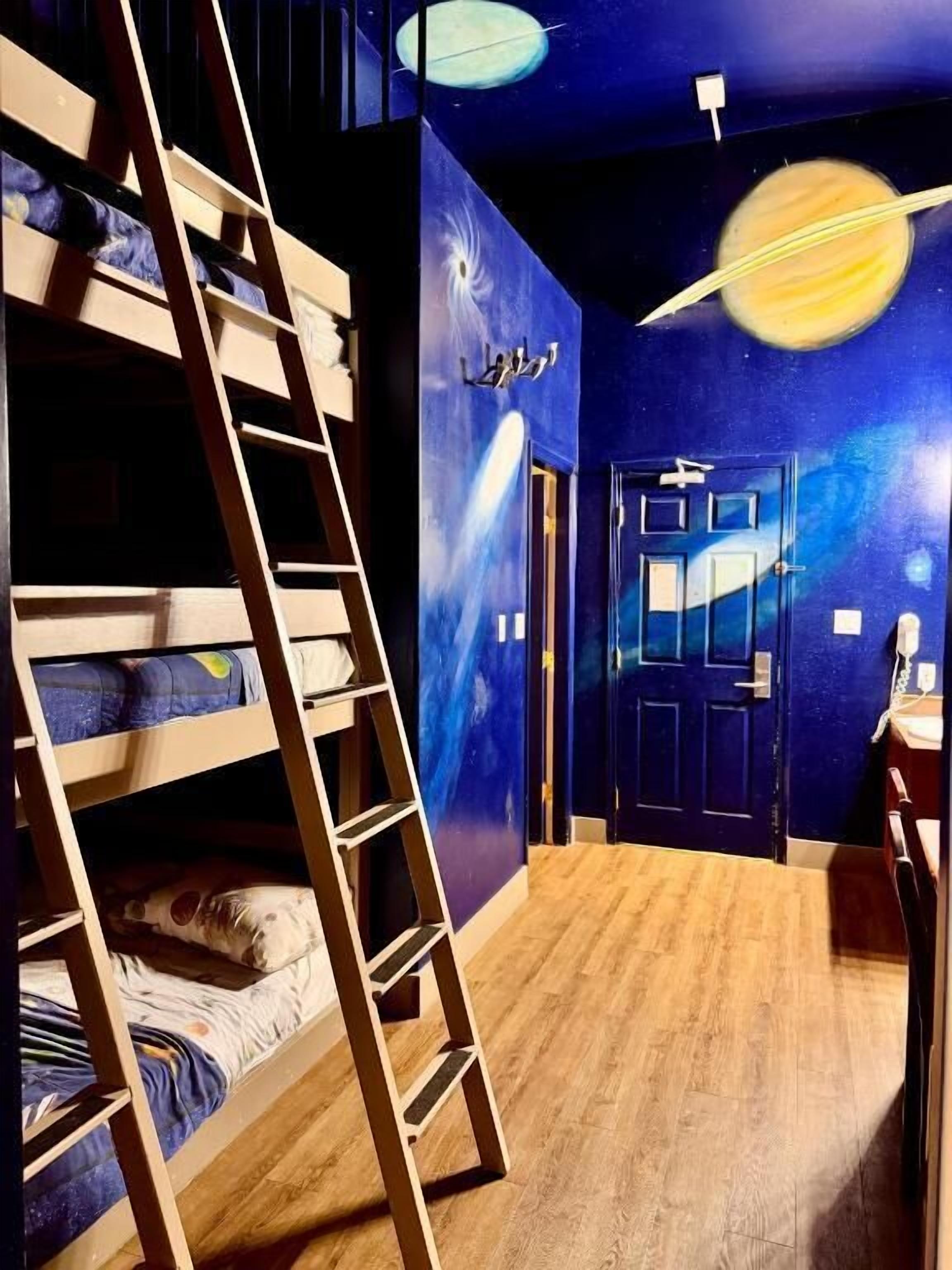 A room with bunk beds, a ladder, a door, and a wall with a space-themed mural.