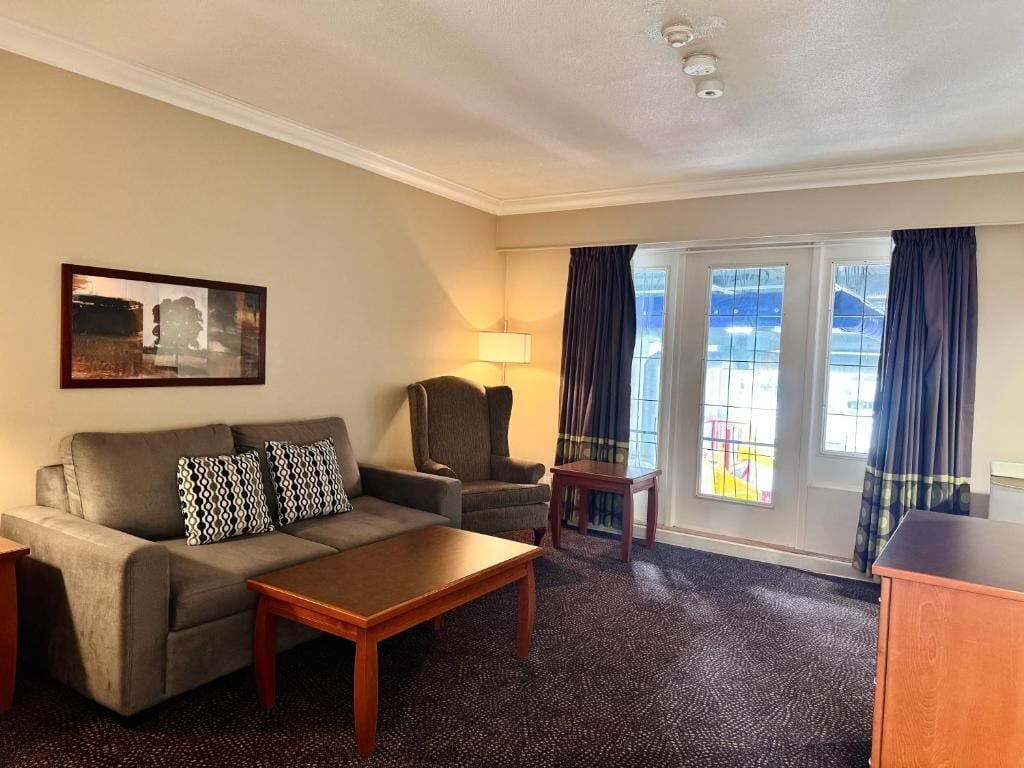 Habitación de hotel con sofá, sillón, mesa de centro y vistas al exterior.