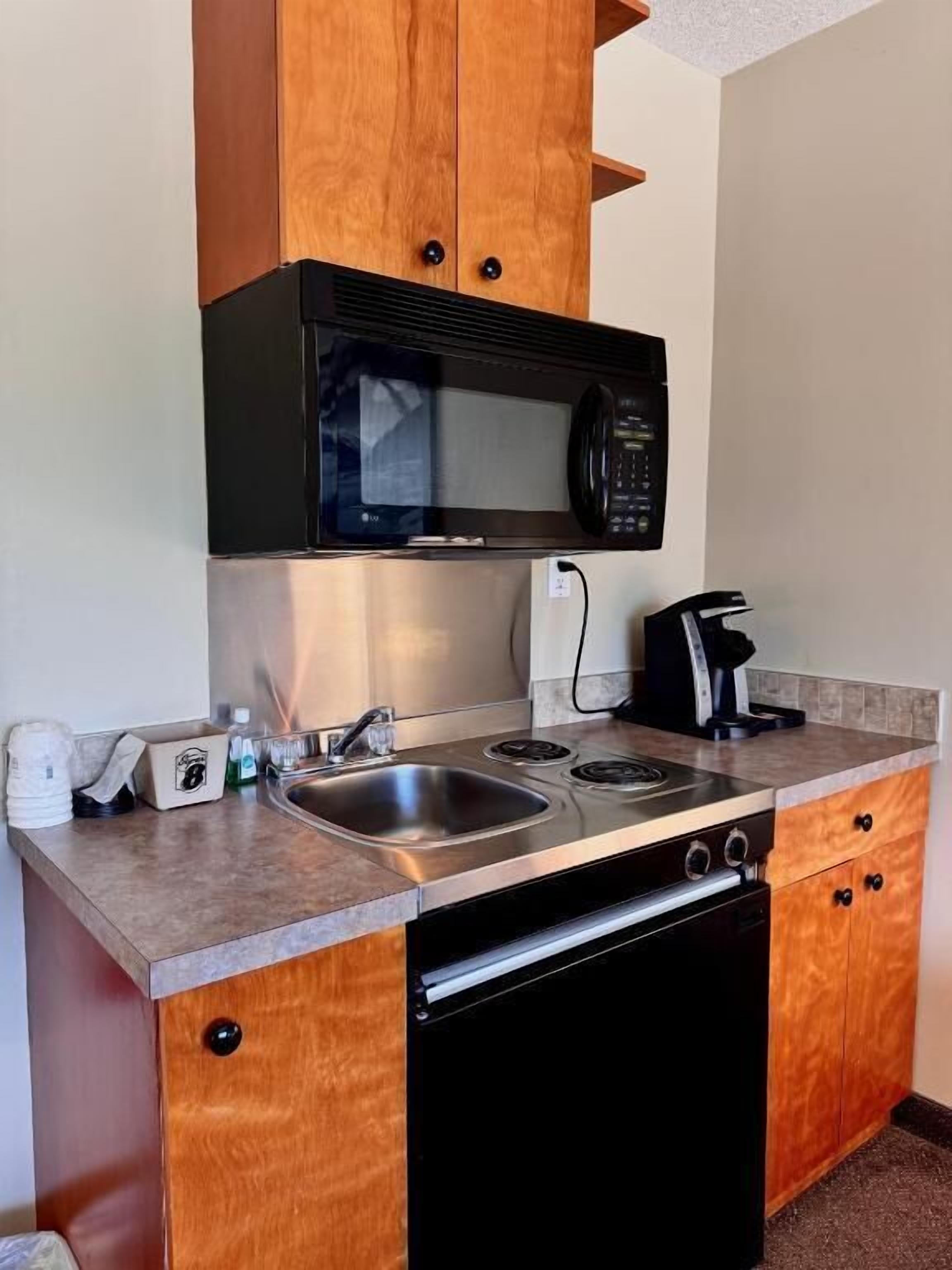 A compact kitchenette with a microwave, stove, sink, and a coffee maker.