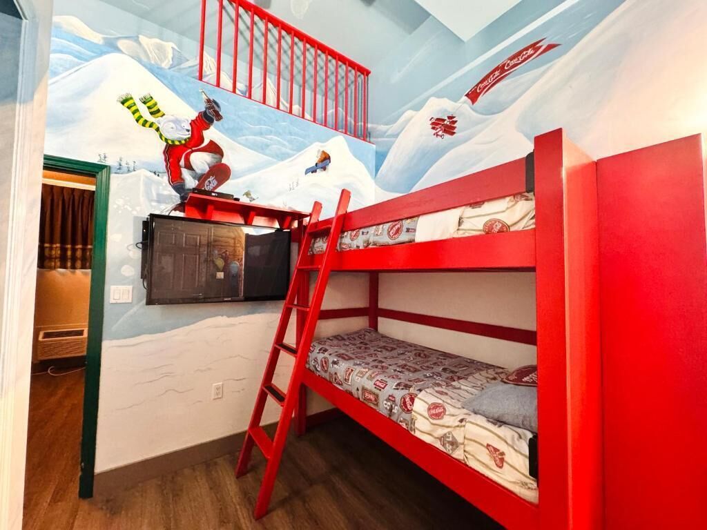 Habitación con literas y un mural de un oso polar y una persona en la montaña, una escalera roja y una ventana pequeña.