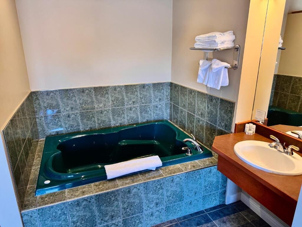 A bathroom with a green bathtub, a white sink, and a mirror.