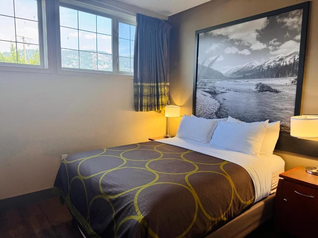 A hotel room with a bed, a nightstand, a window with curtains, and a large framed picture on the wall.