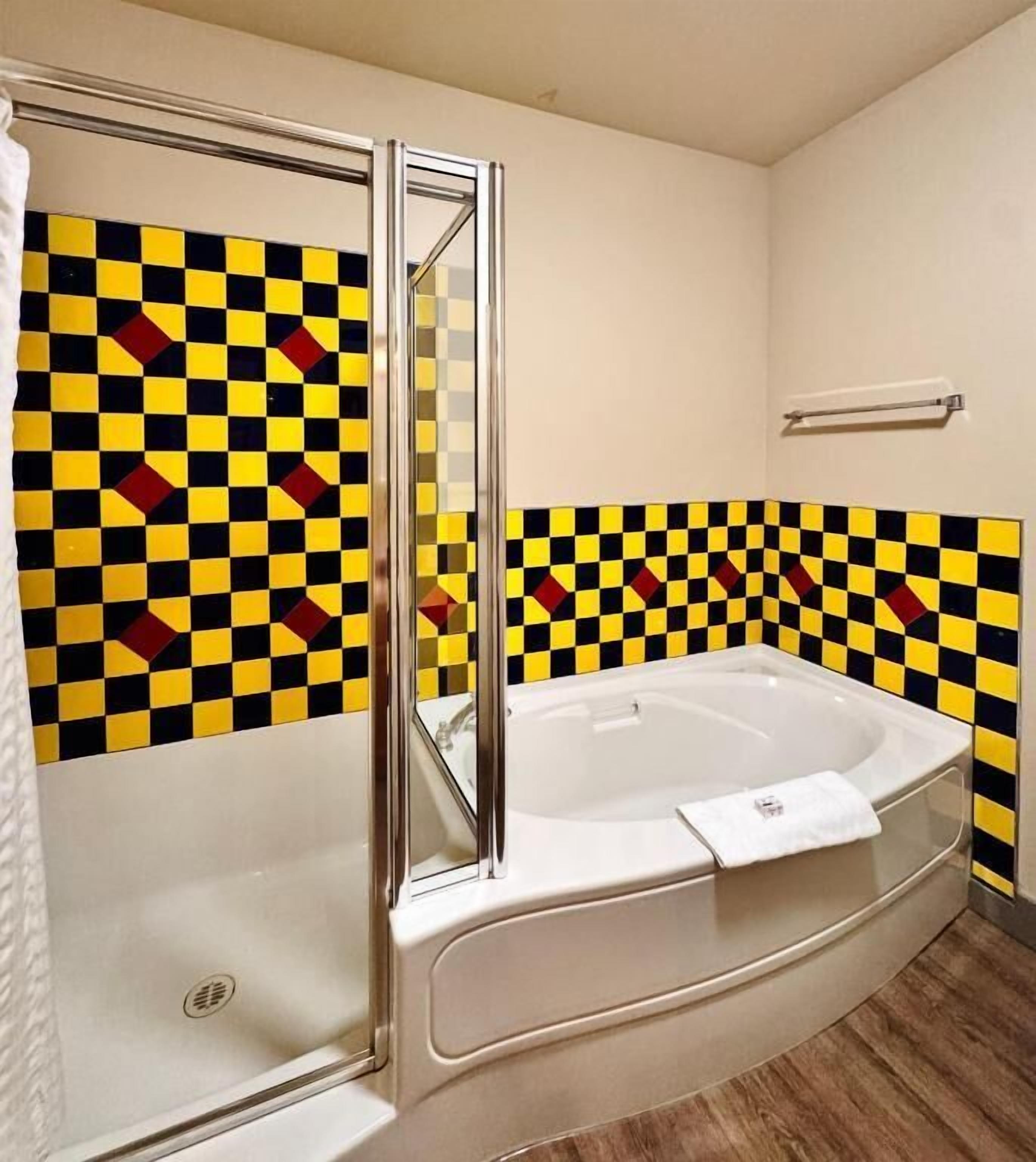A bathroom with a checkered tile wall, a white bathtub, and a glass shower enclosure.