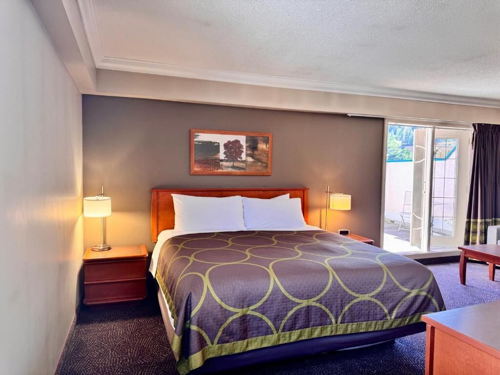 Camera d'albergo con un letto grande, due lampade ai comodini, un quadro appeso al muro e vista attraverso la porta in vetro.