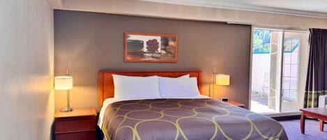 Camera d'albergo con un letto grande, due lampade ai comodini, un quadro appeso al muro e vista attraverso la porta in vetro.