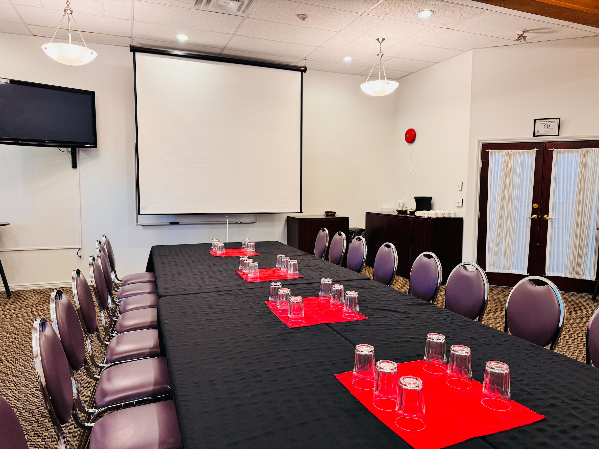 A conference room with a long table, chairs, a projector screen, and a red carpet.