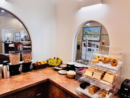 Un mostrador de desayuno con diversas opciones de comida, una máquina de café y vistas de la ciudad a través de un ventanal arqueado.