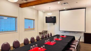 Un salón de conferencias con una larga mesa, sillas, una pantalla de proyector y un televisor.