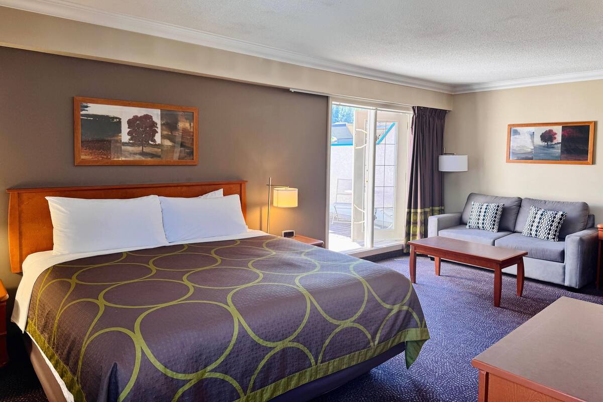 A hotel room with a large bed, a sofa, a coffee table, and a sliding glass door leading to an outdoor area.