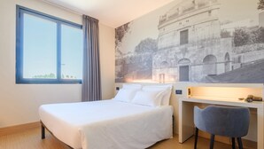 A hotel room with a bed, a desk, and a chair. There is a window with a view of a building. - B&B Hotel Ravenna (Ravenna)