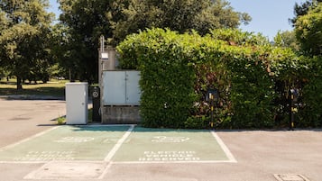 Un área de estacionamiento con estaciones de carga para vehículos eléctricos, una caja de servicios y un seto.