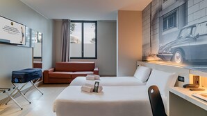 A hotel room with a bed, a desk, a chair, a sofa, a window, and a wall-mounted TV. - B&B Hotel Ravenna (Ravenna)