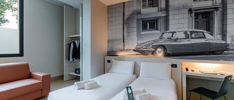 A hotel room with two beds, a desk, a chair, a wardrobe, and a large window.