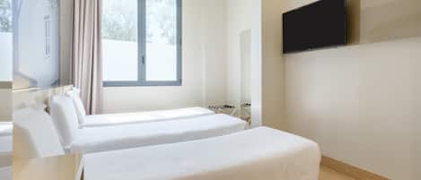 Habitación de hotel con dos camas, un televisor montado en la pared y una ventana con cortinas.