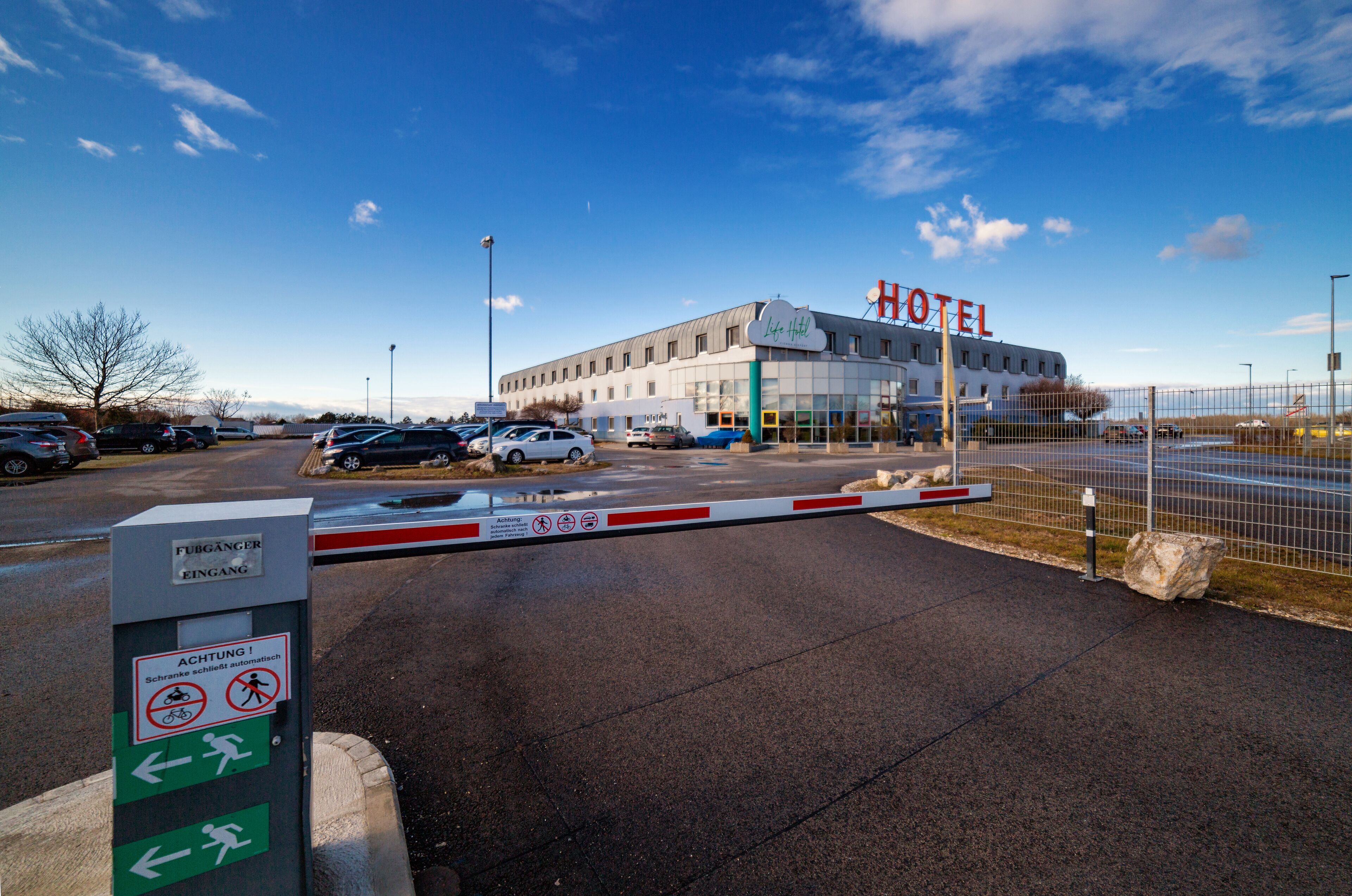A hotel entrance with a gated driveway, a sign indicating no bicycles or wheelchairs, and a clear sky.