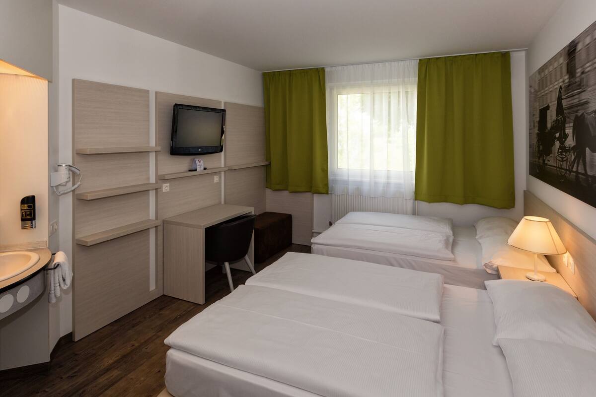 A hotel room with two beds, a desk, a TV, and a bathroom.