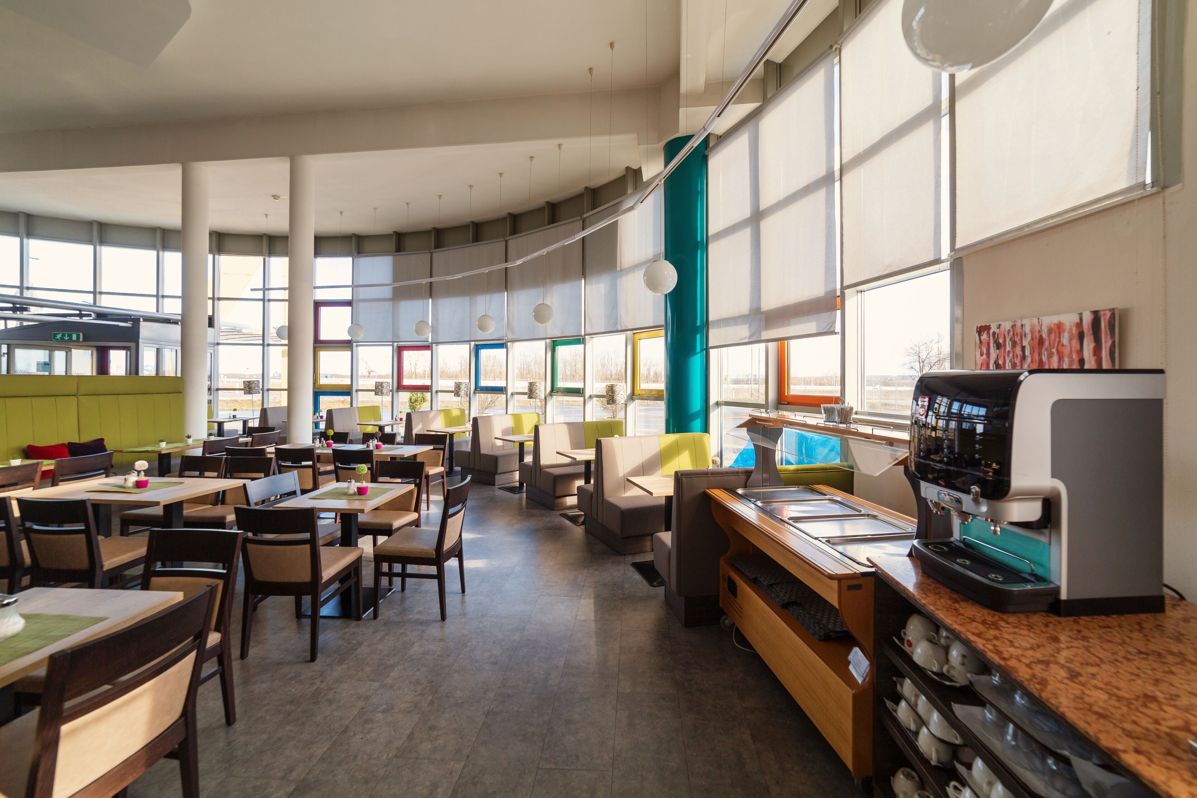 Un café moderno con varias zonas de estar, incluyendo mesas y cabinas, y una máquina de café en la barra.
