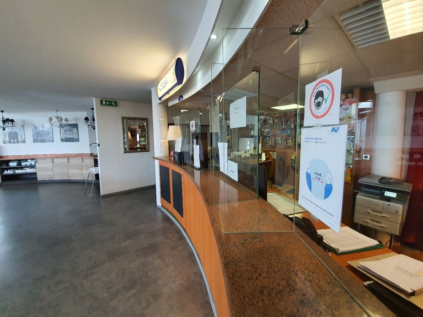 A reception area with a curved counter, glass partitions, and a visible exit sign.