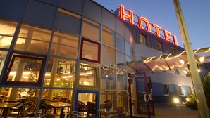 A hotel with a modern glass facade, a neon sign, and outdoor seating area. - Life Hotel (Fischamend)