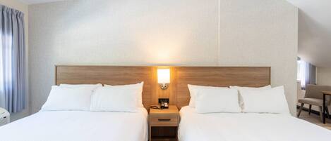 Habitación de hotel con dos camas, una mesita de noche con lámpara, un escritorio y una silla.