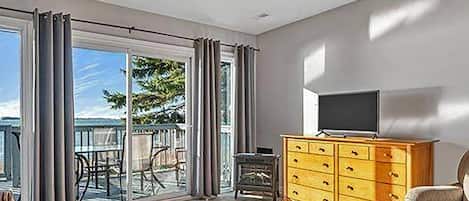 Ein Zimmer mit einer Couch, einem Fernseher auf einer Holzkommode und einem Balkon mit Gartenmöbeln.