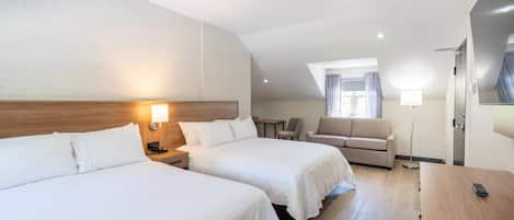A hotel room with two beds, a desk, a chair, a sofa, and a large window.