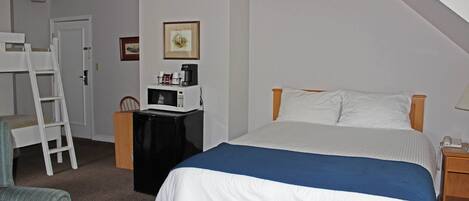 A bedroom with a bed, a desk with a microwave, a chair, and a ladder.