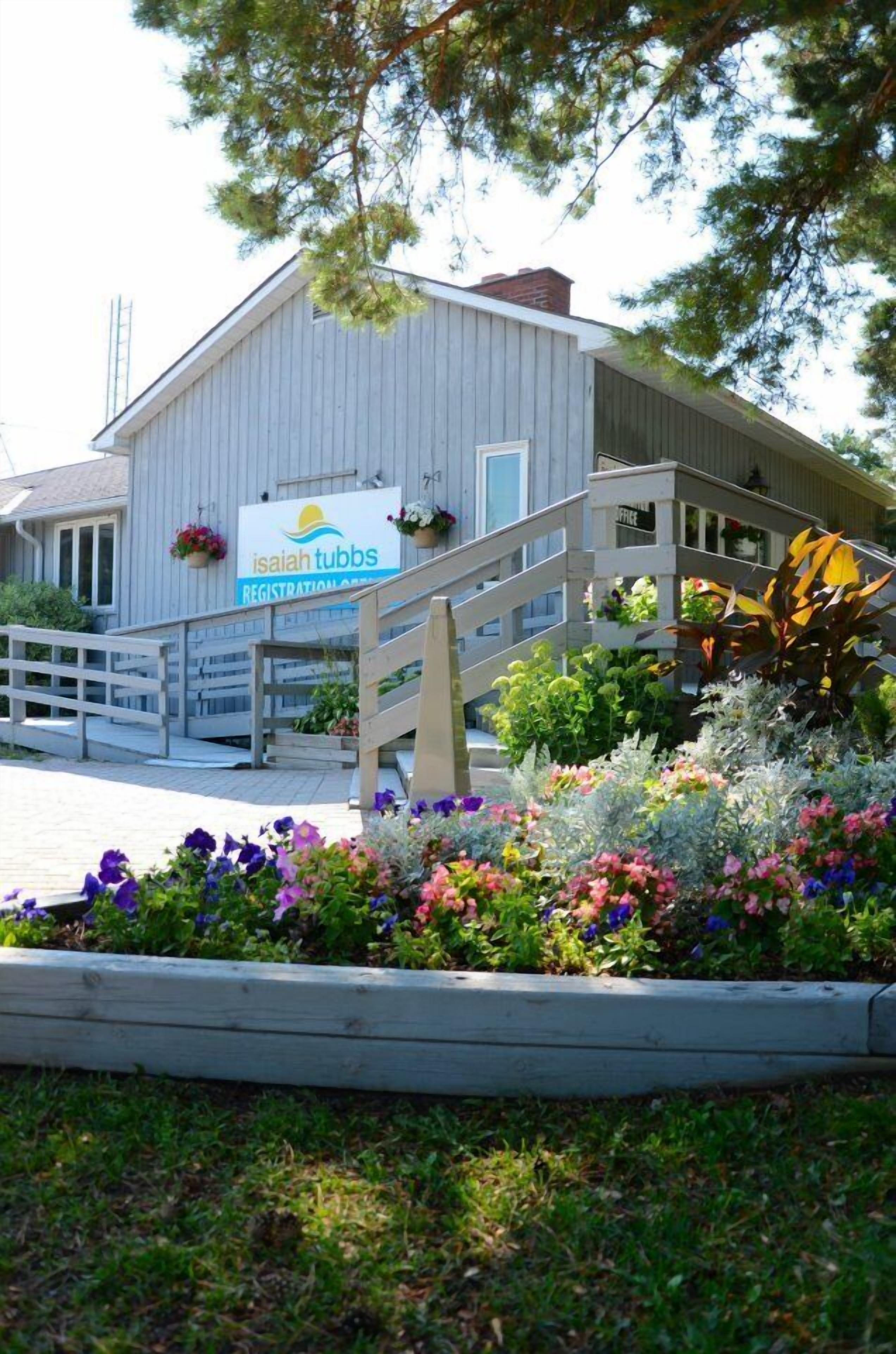A building with a sign for Isaiah Tubbs Registration Office, a wooden staircase, and a flower bed with various flowers.