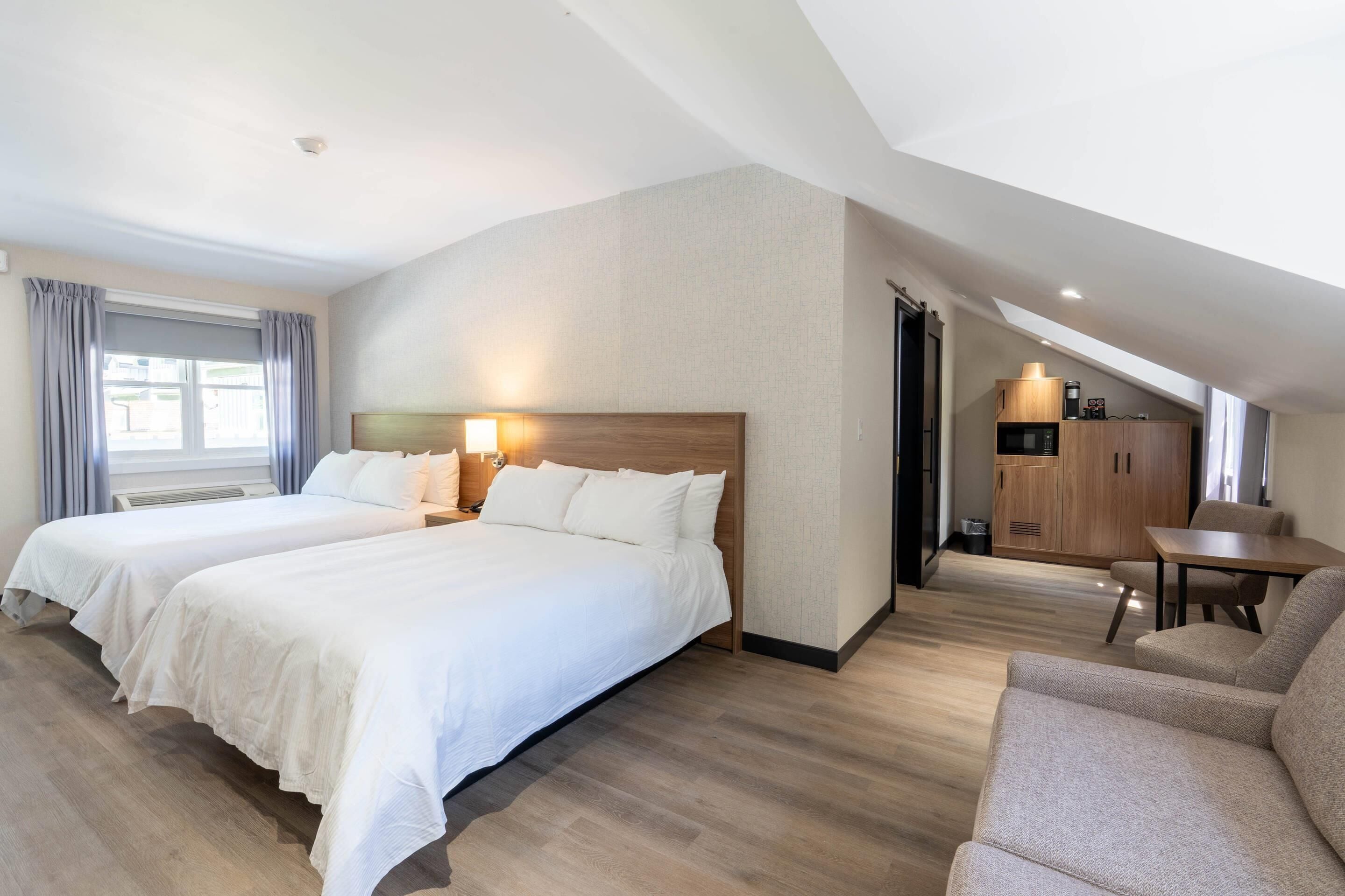 A hotel room with two beds, a sofa, a dining table, and a kitchenette.