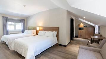 A hotel room with two beds, a sofa, a dining table, and a kitchenette.