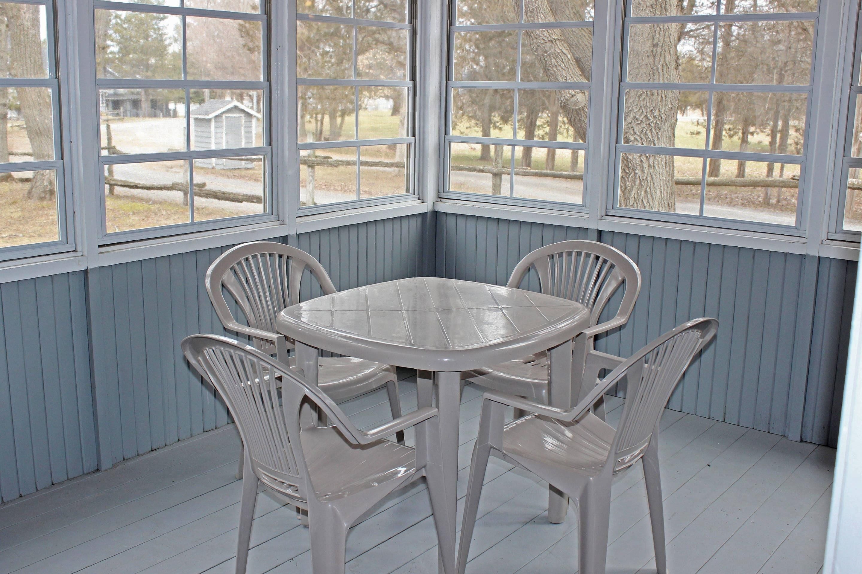 A corner room with a round table and four chairs, large windows, and a view of the outdoors.