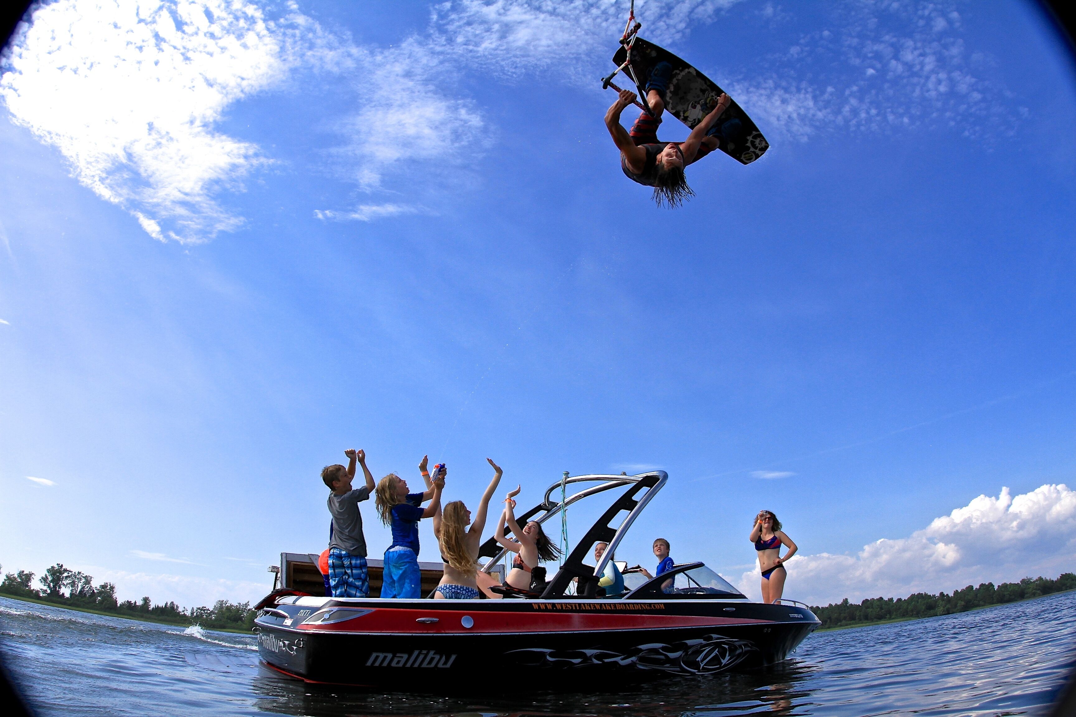 Ein Boot mit Personen an Bord, ein Wakeboarder in Aktion und ein klarer, blauer Himmel.
