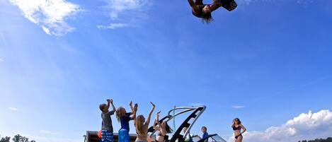 Ein Boot mit Personen an Bord, ein Wakeboarder in Aktion und ein klarer, blauer Himmel.