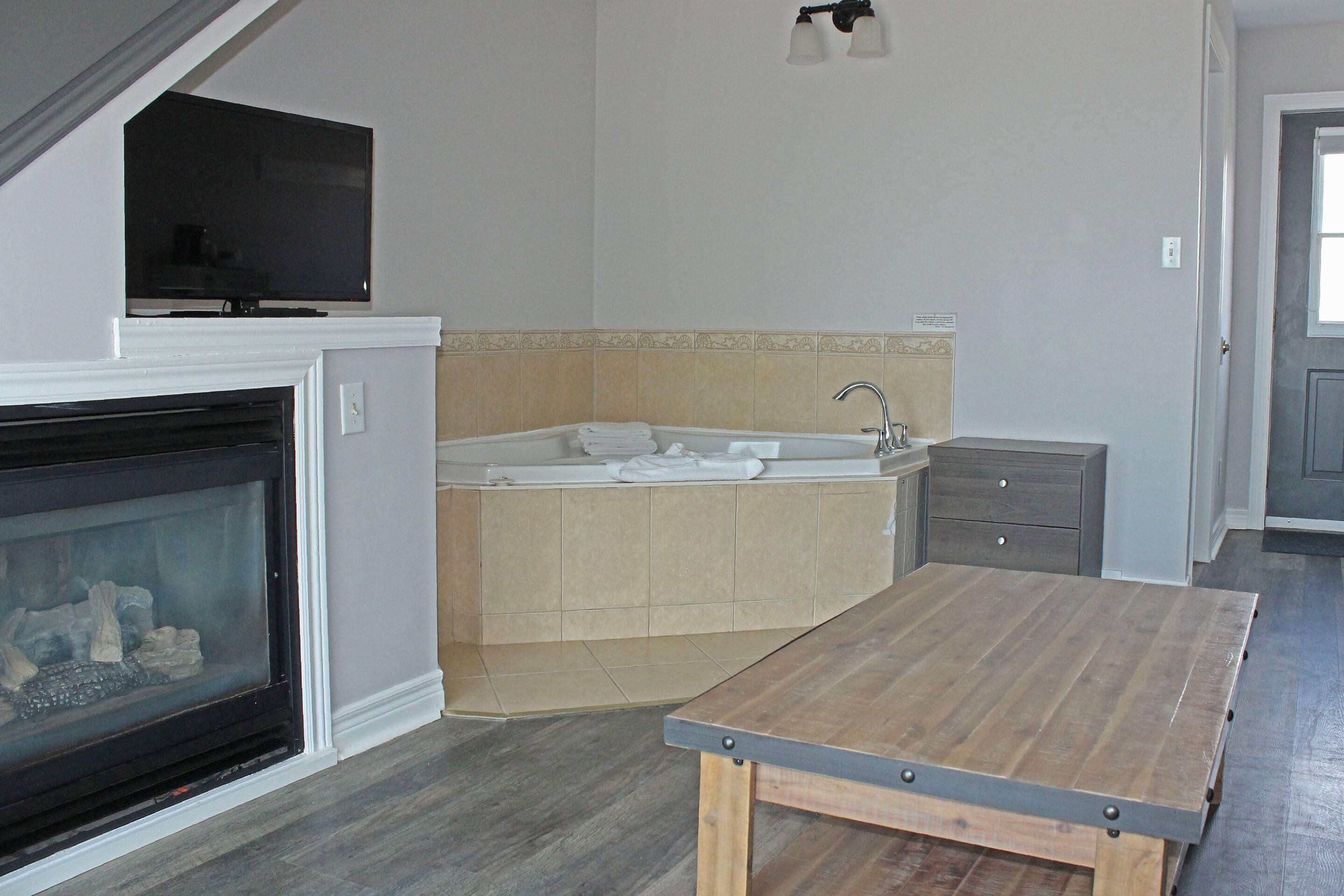 Ein Zimmer mit Kamin, Fernseher, Badewanne und einem Holztisch.