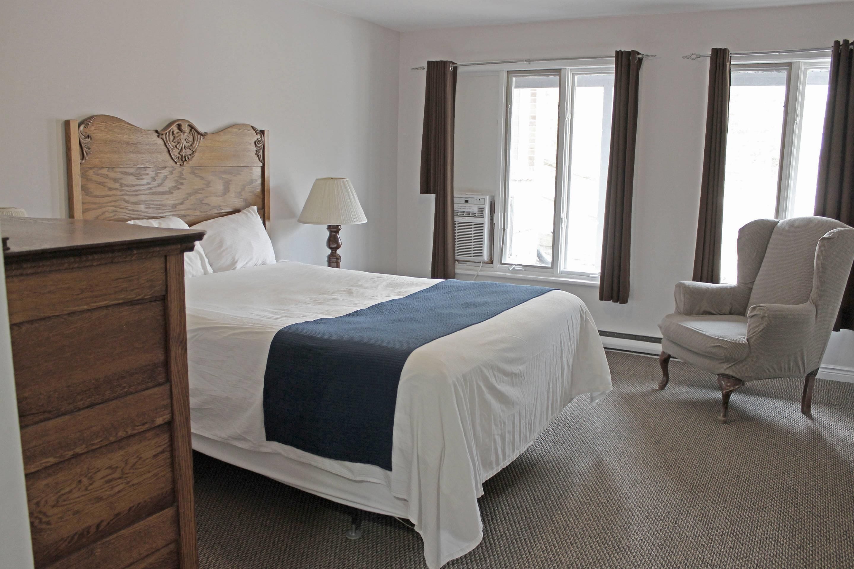 A hotel room with a bed, a chair, a dresser, a lamp, and a window with curtains.
