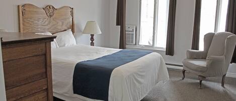 A hotel room with a bed, a chair, a dresser, a lamp, and a window with curtains.