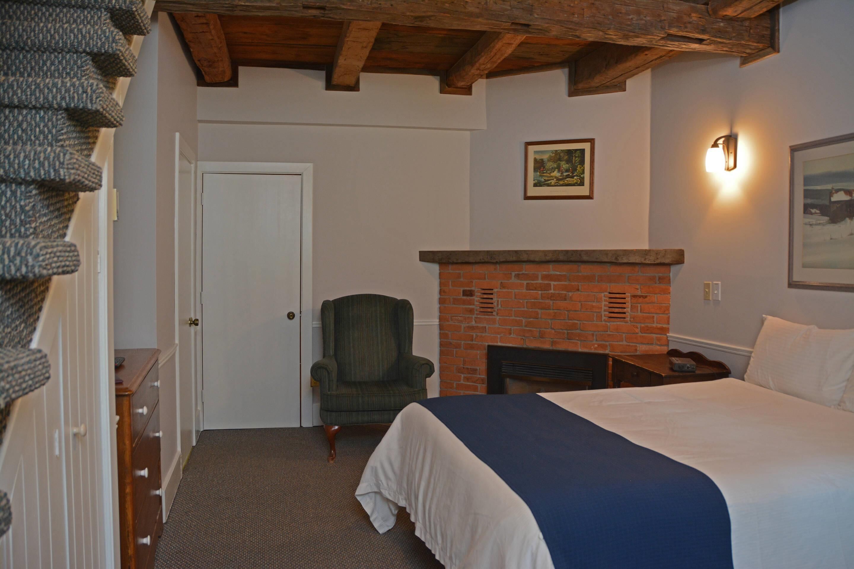Ein Schlafzimmer mit Bett, Kamin, Stuhl, einer Tür und einer Wandleuchte.