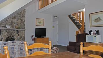 A living room with a stone wall, a television, a staircase, and a dining area with wooden furniture.