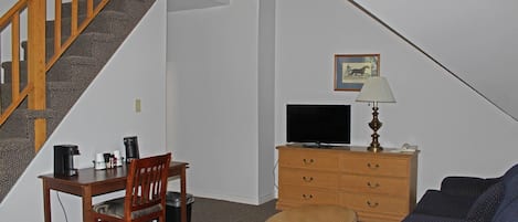 Una escalera que conduce a un altillo, un escritorio con una silla, un televisor, una lámpara y un sofá.