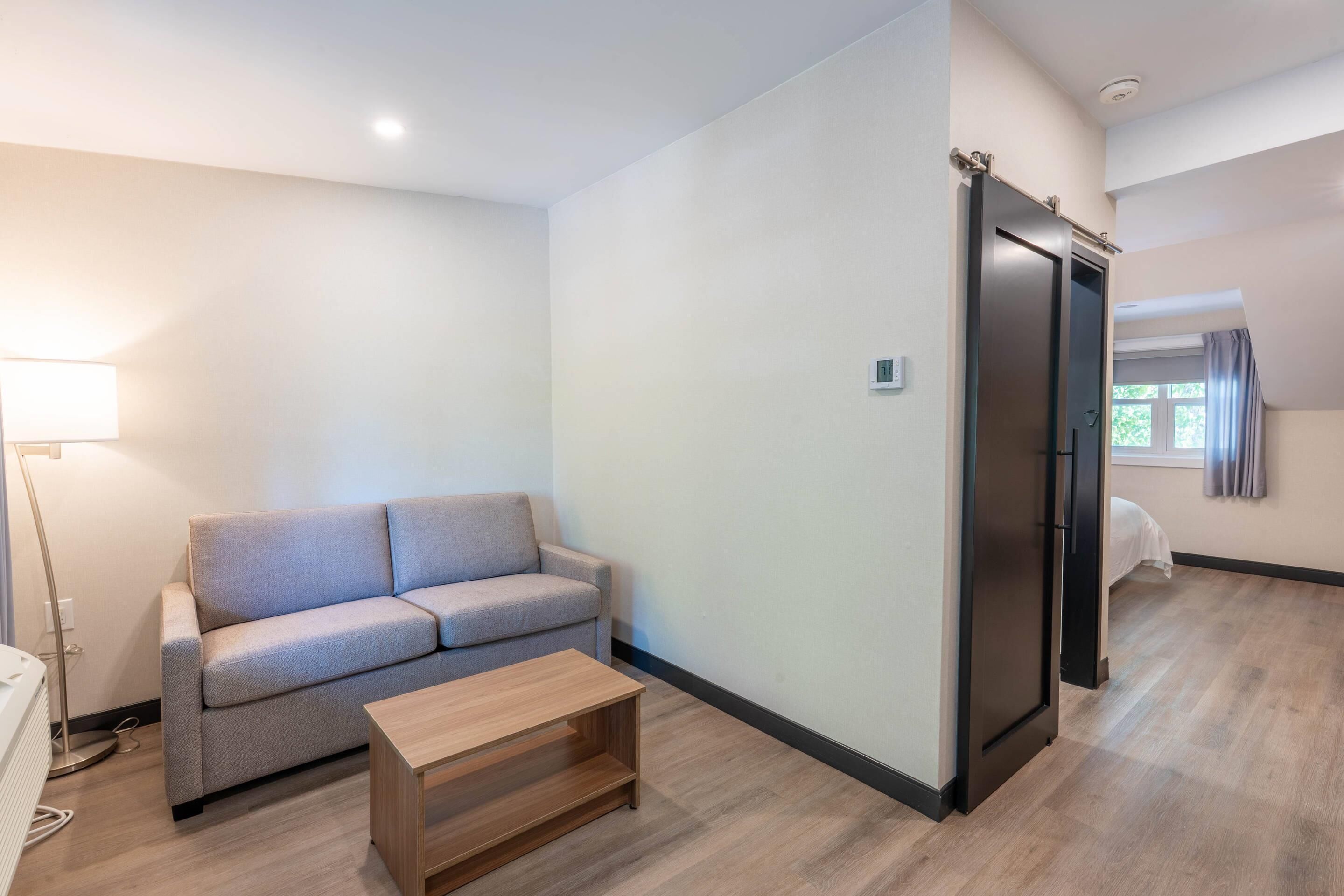 A modern living room with a sofa, a coffee table, a lamp, and a door leading to another room.
