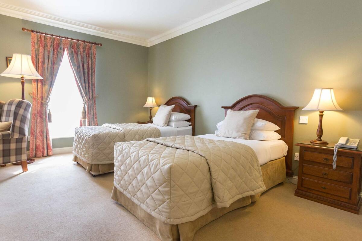 A hotel room with two beds, a chair, a nightstand, and a lamp.