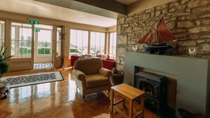 A spacious living room with a stone fireplace, a red sailboat decoration, a comfortable armchair, and a large window offering a view of the outdoors. - Sheedy's Country House Hotel (Lisdoonvarna)