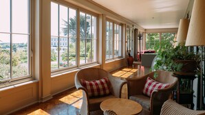 A sunlit room with large windows, wicker furniture, and a potted plant. - Sheedy's Country House Hotel (Lisdoonvarna)