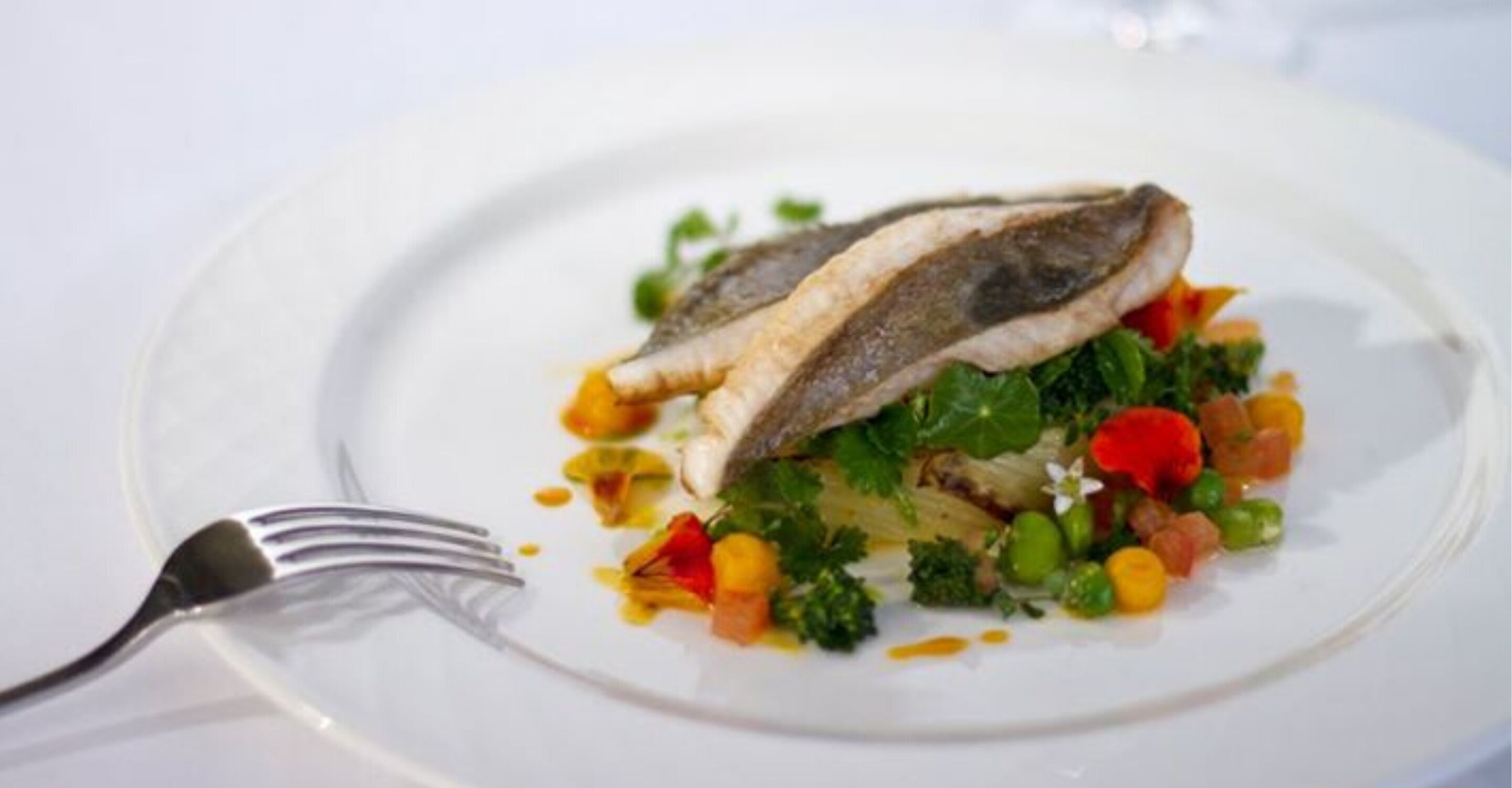 A plate with a fish, vegetables, and a fork.