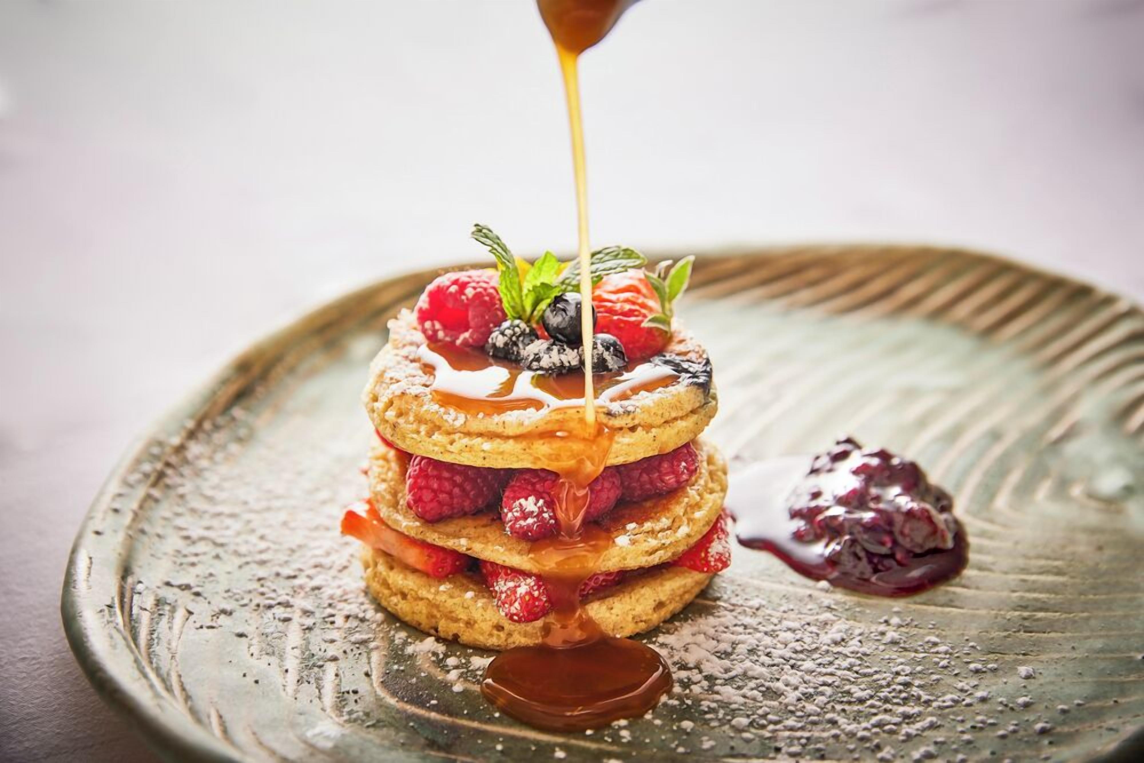 A stack of pancakes with berries and syrup on a ceramic plate.