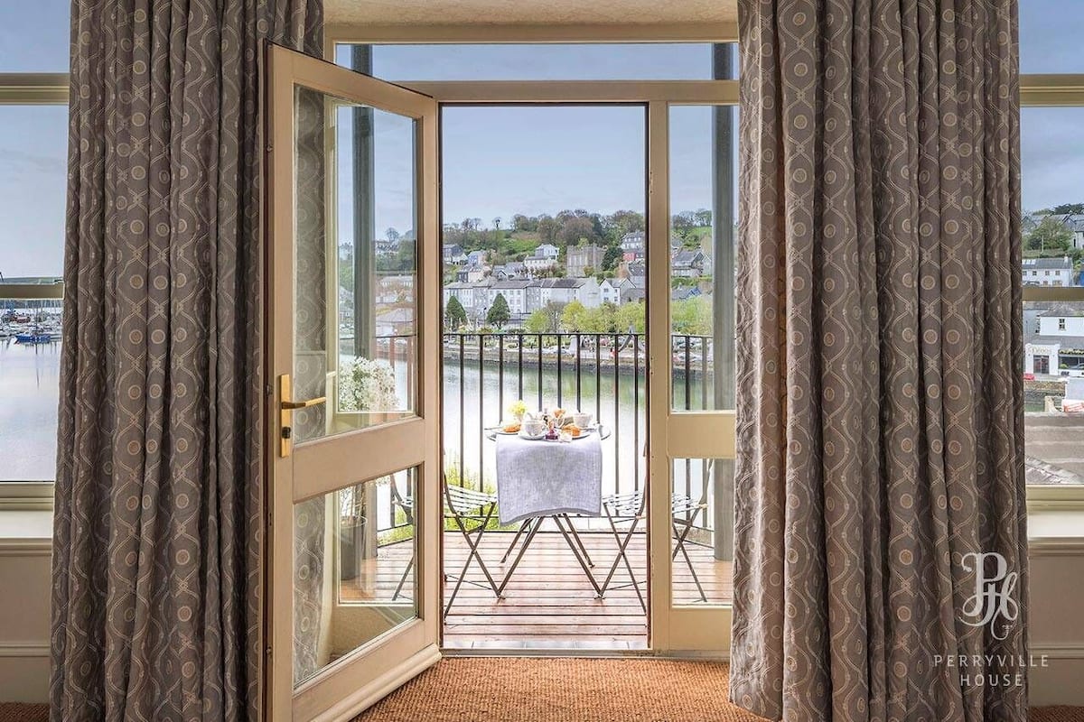 A balcony with a table and chairs, overlooking a body of water and a town.